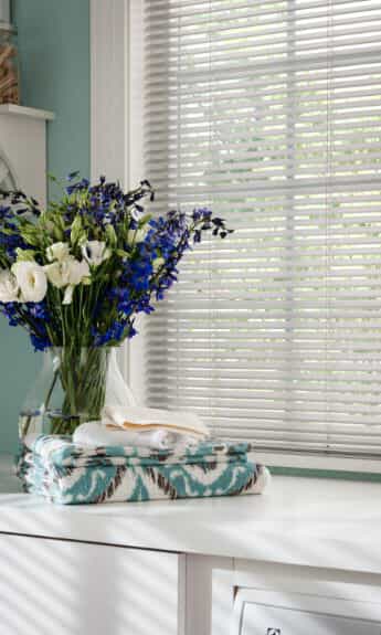 A vase on a countertop with horizontal blinds visible through the window behind.